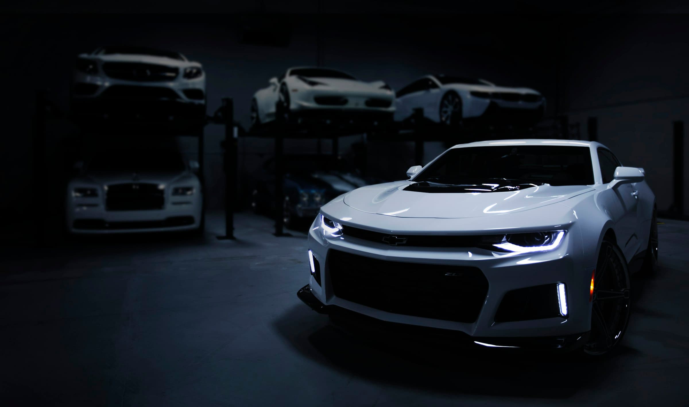 Camaro branco com faróis acesos numa garagem escura